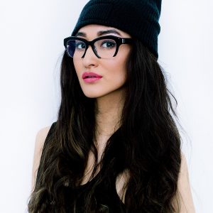 Brunette girl wearing stylish eyeglasses with thick frame and beanie cap.